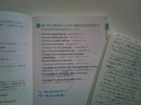 ページを開いた状態の「ビジネス英語　ライディング表現」の本と、英語の例文がたくさん書かれた白い紙が並んでいる