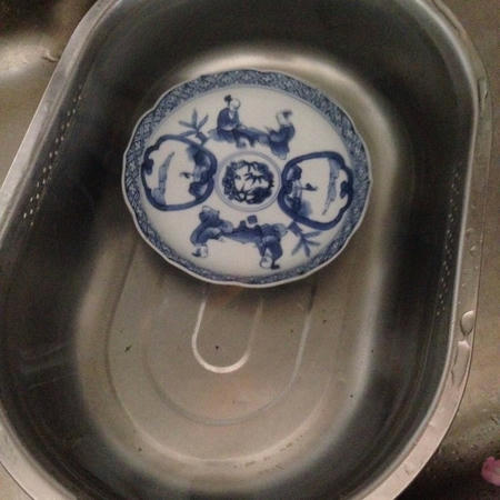 金属製の大きな水桶に透明な水道水が張られ、その中に中華風の絵の描かれた青い皿1枚が沈んでいる画像