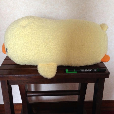 全長43cmの黄色いひよこの抱き枕（ぬいぐるみ）と黄緑色の蛍光ペンを木製の台の上に置き、横から撮った写真。ひよこのぬいぐるみは、「マザーガーデン」のぴよちゃんの抱き枕のちびサイズ。